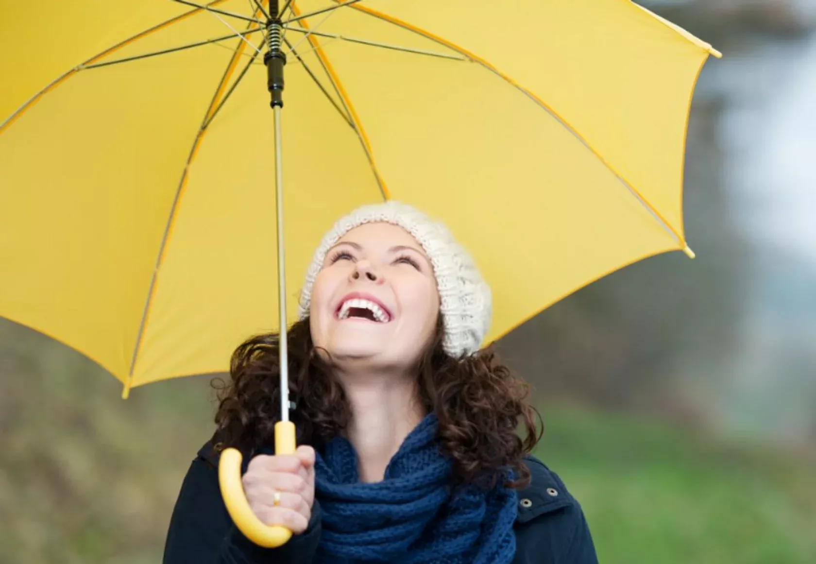Frau mit gelbem Regenschirm lacht trotz schlechten Wetters.
