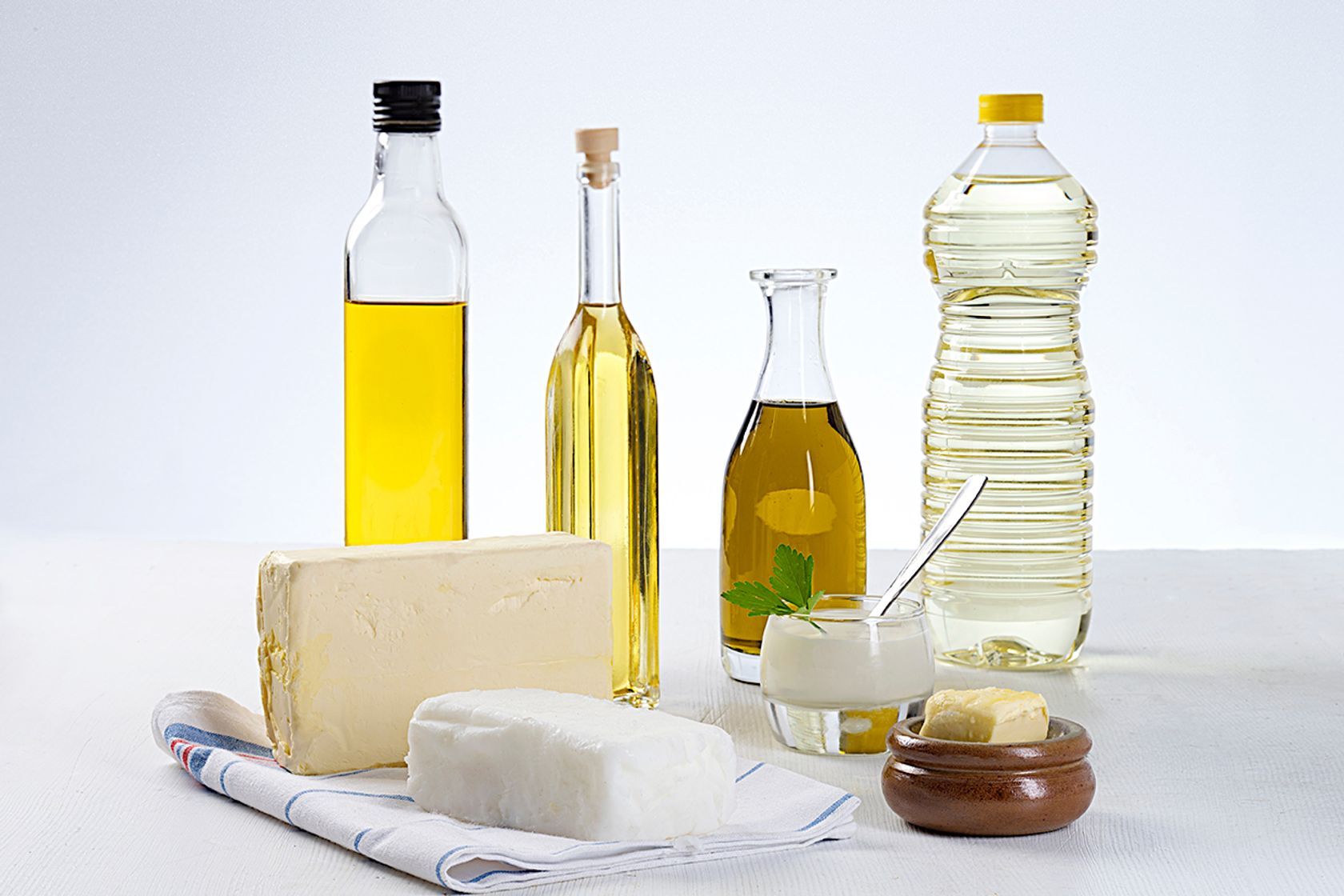 Kokosöl, Margarine, je eine Flasche Olivenöl, Rapsöl, Sonnenblumenöl stehen auf einer Fläche.