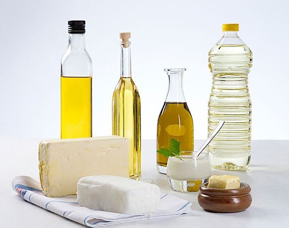Kokosöl, Margarine, je eine Flasche Olivenöl, Rapsöl, Sonnenblumenöl stehen auf einer Fläche.