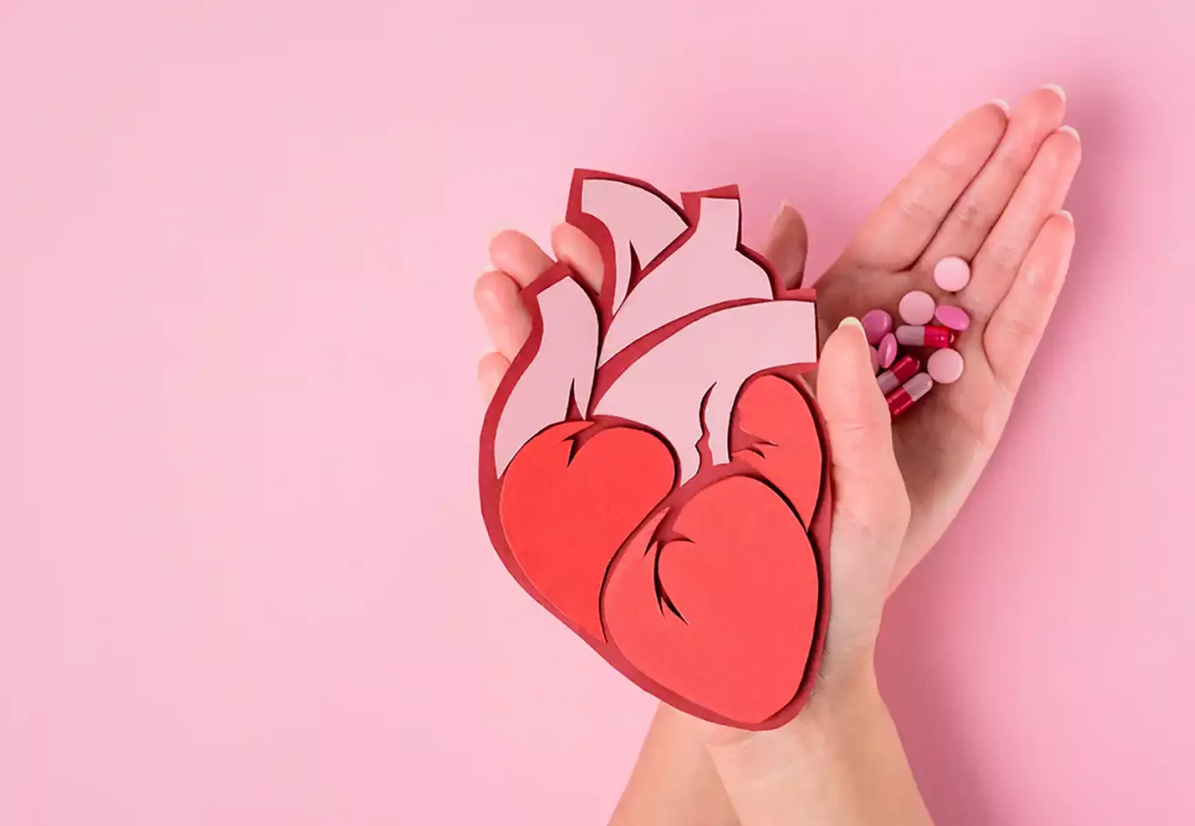 Zwei Hände halten ein Modell eines Herzens und Kapseln mit Nahrungsergänzungsmitteln.