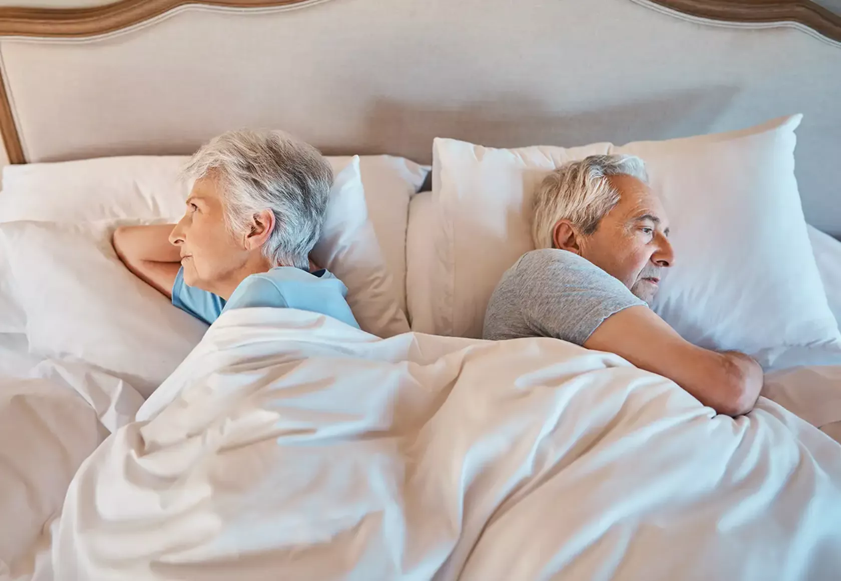 Älteres Paar liegt im Bett und wendet sich den Rücken zu.