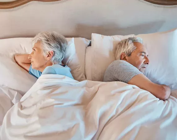 Älteres Paar liegt im Bett und wendet sich den Rücken zu.