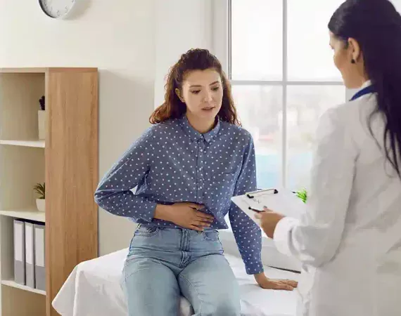 Junge Frau schildert einer Ärztin ihre Bauch-Beschwerden.