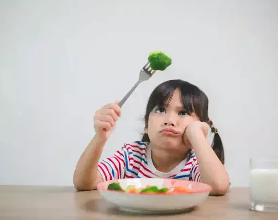 Kleines Mädchen schaut unlustig auf ein Stück Brokkoli, das sie auf der Gabel hat.