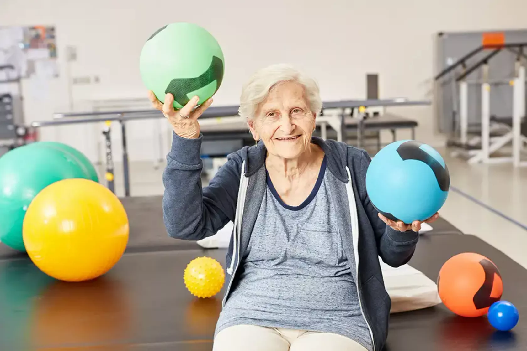 Eine Seniorin macht im Fitnessstudio Übungen mit Bällen.