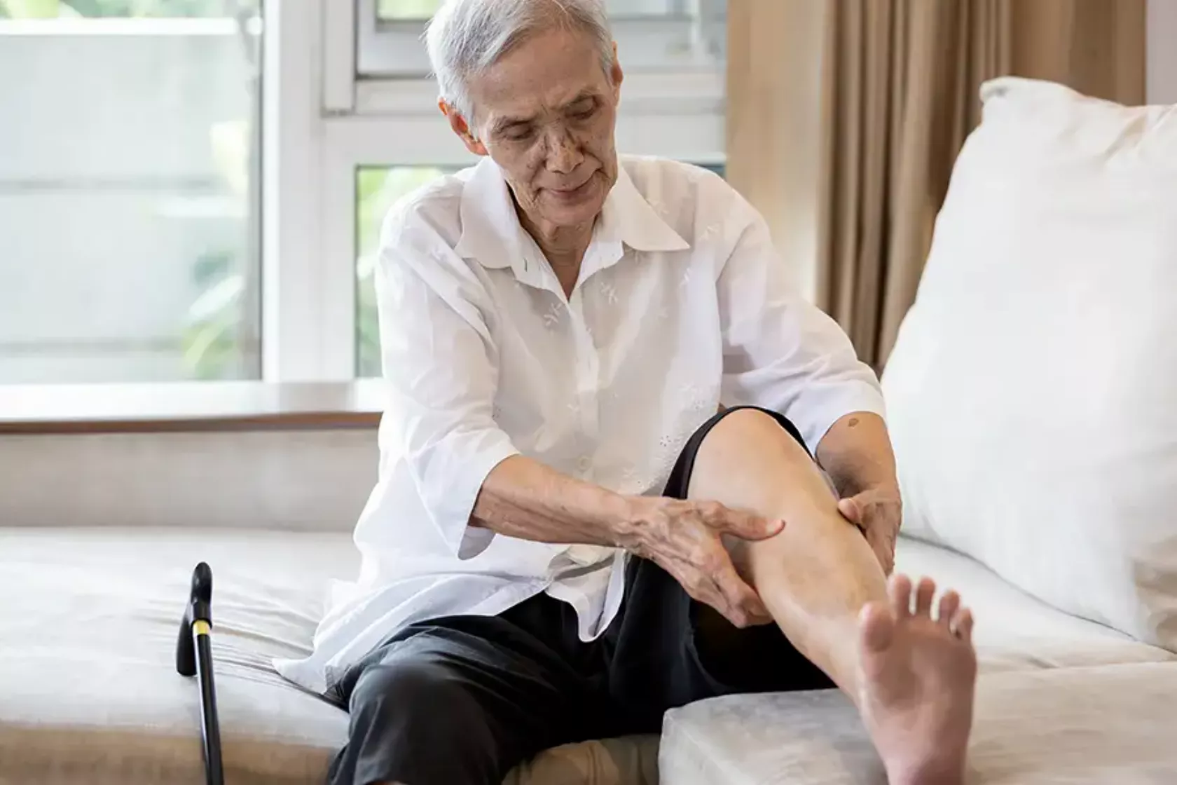 Ein alter Herr im Pflegeheim betastet sein hochgelegtes Bein am Unterschenkel.