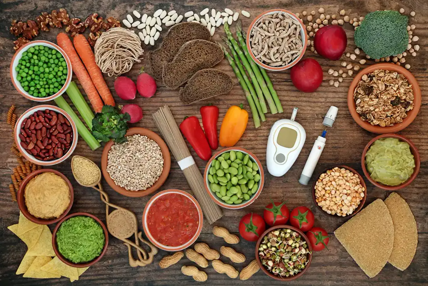 Viele Nahrungsmittel, Gemüse, Gewürze, Kräuter und ein Blutglukosemessgerät auf einem Tisch von oben gesehen.