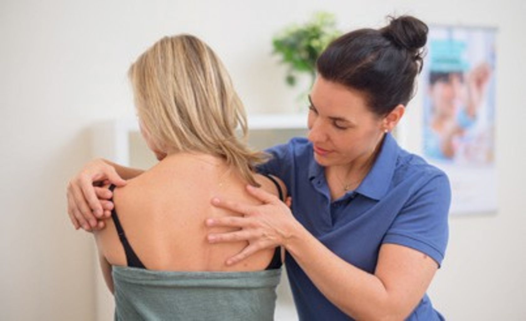 Eine Osteopathin behandelt im Sitzen die Schulter einer Frau.
