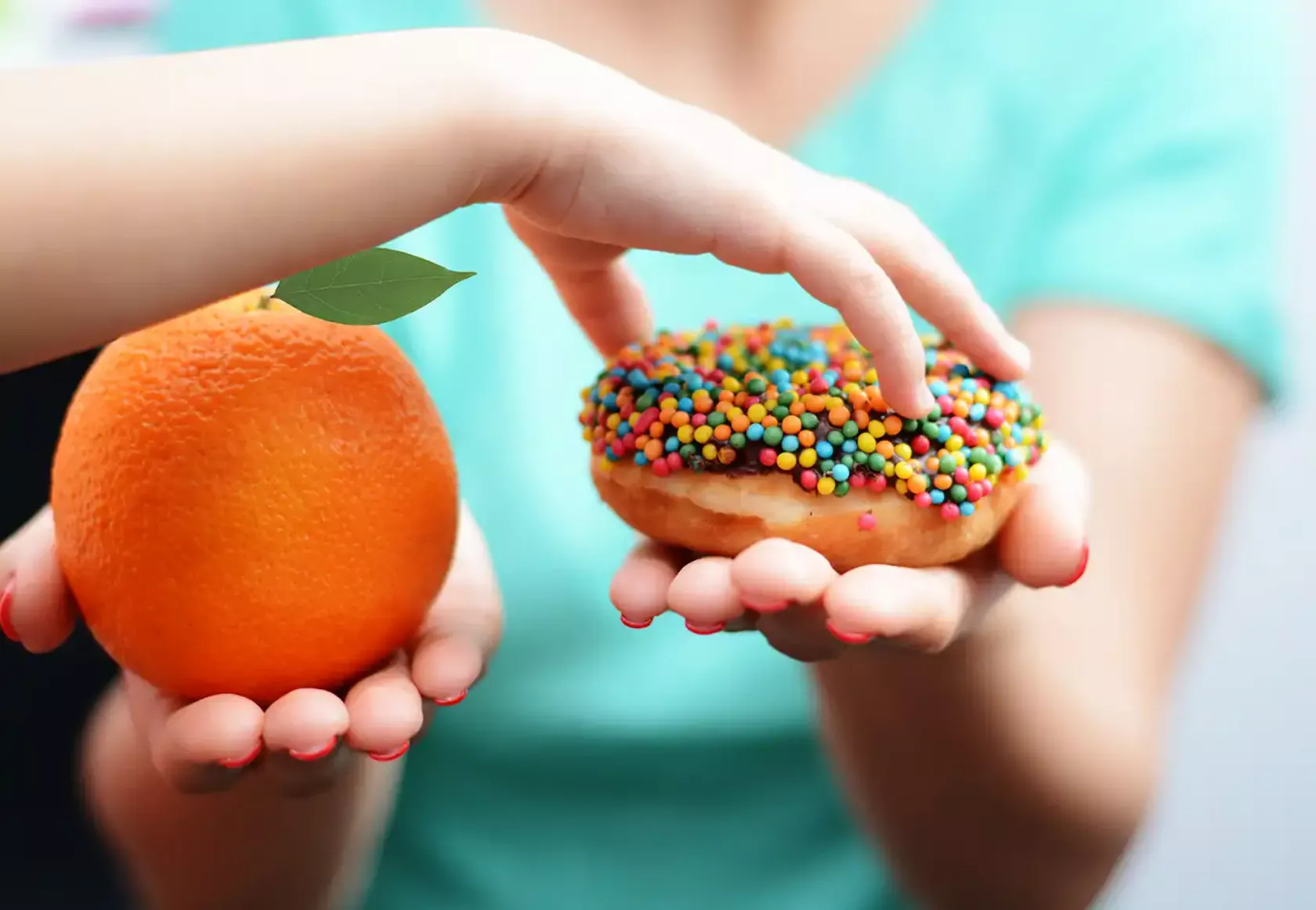 Einem Kind wird eine Orange und ein Donut hingehalten, es greift nach dem Donut.