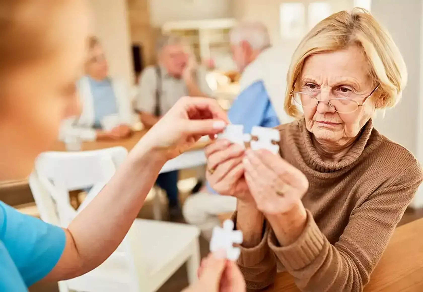 Eine Seniorin trainiert mit einer Therapeutin, ein Puzzle zusammenzusetzen.