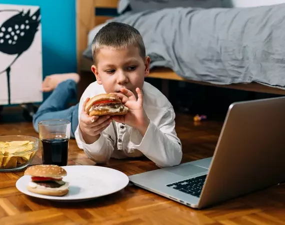 Junge mit seinem Laptop und isst Burger und trinkt Cola.