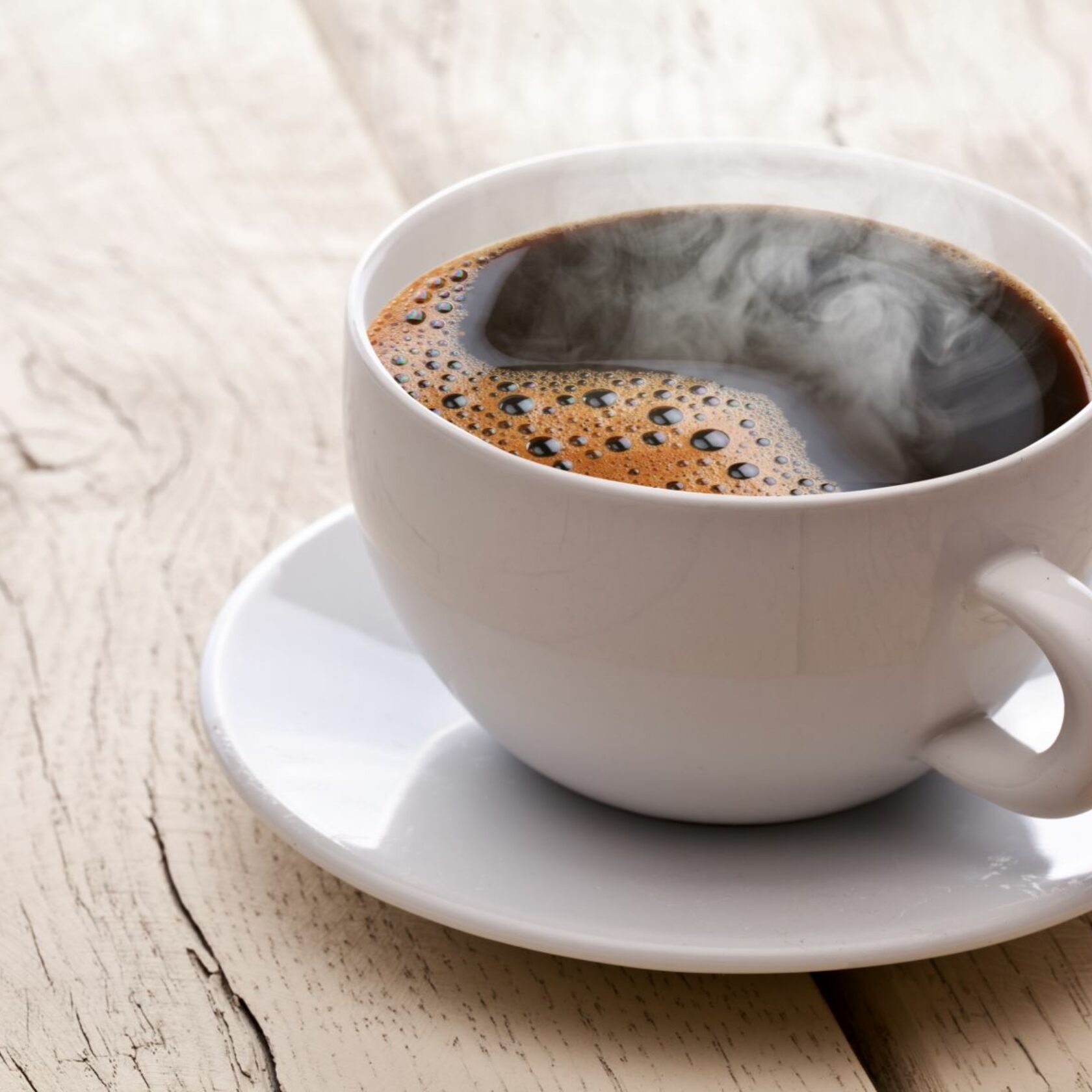 Eine dampfende Tasse Kaffee steht auf einem Holztisch.